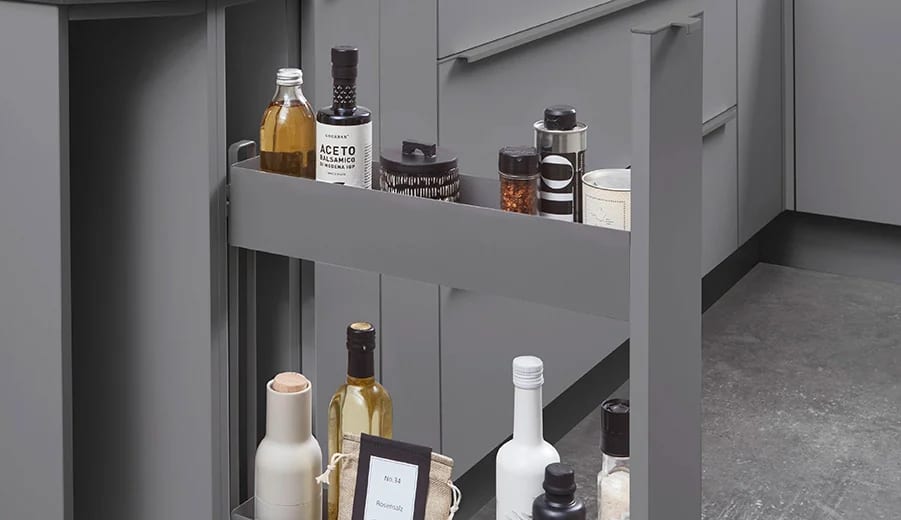 Coulissant étroit sorti entre deux meubles gris, deux paniers superposés portant huiles, vinaigres et épices