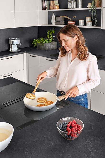 Une personne cuisine sur une table de cuisson à hotte intégrée, sans meuble ni hotte suspendue au-dessus de la tête