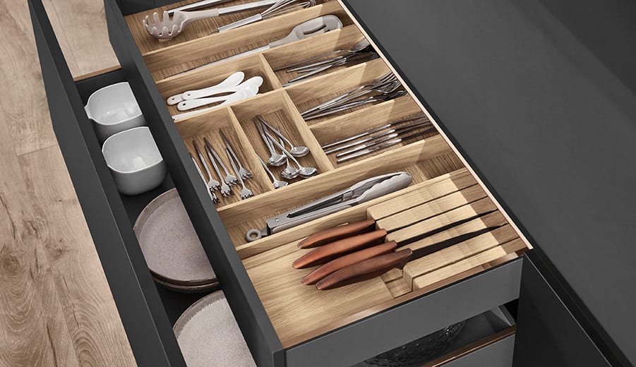 Tiroir de cuisine anthracite ouvert, range-couverts en bois massif compartimenté, bols et assiettes dans le tiroir voisin