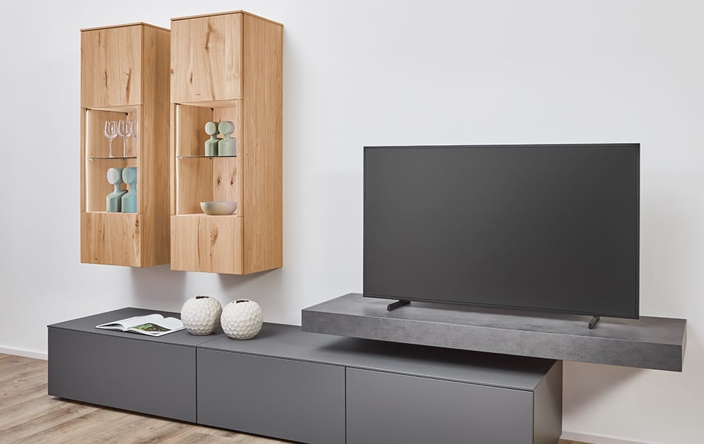 Deux éléments hauts à portes vitrées dont l’intérieur est en décor chêne, au-dessus d’un meuble bas gris anthracite dont la joue est visible