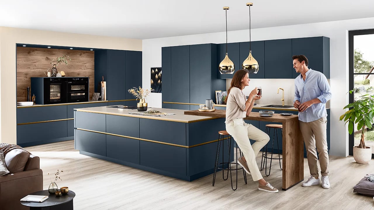 Cuisine en laque ultra-mate bleu profond, profilés et suspensions laiton, îlot avec table en bois