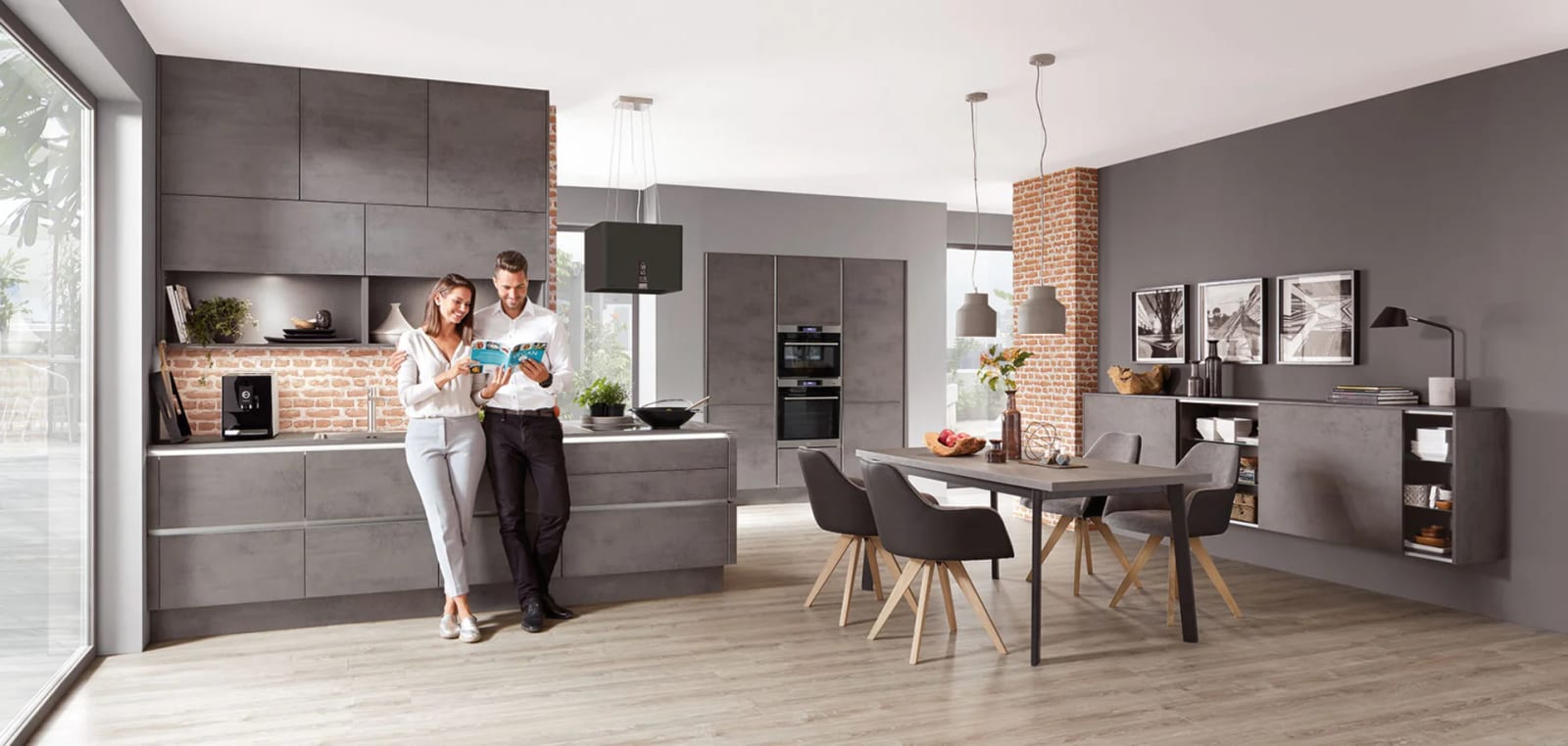 Cuisine linéaire en décor béton gris, colonnes jusqu’au plafond, mur de brique apparente et coin repas ouvert