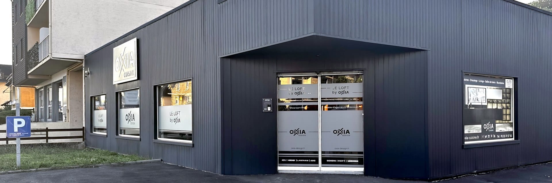 La façade anthracite du showroom OXIA, 122 avenue Ribot à Brive-la-Gaillarde, son enseigne éclairée et sa porte vitrée sous l’auvent