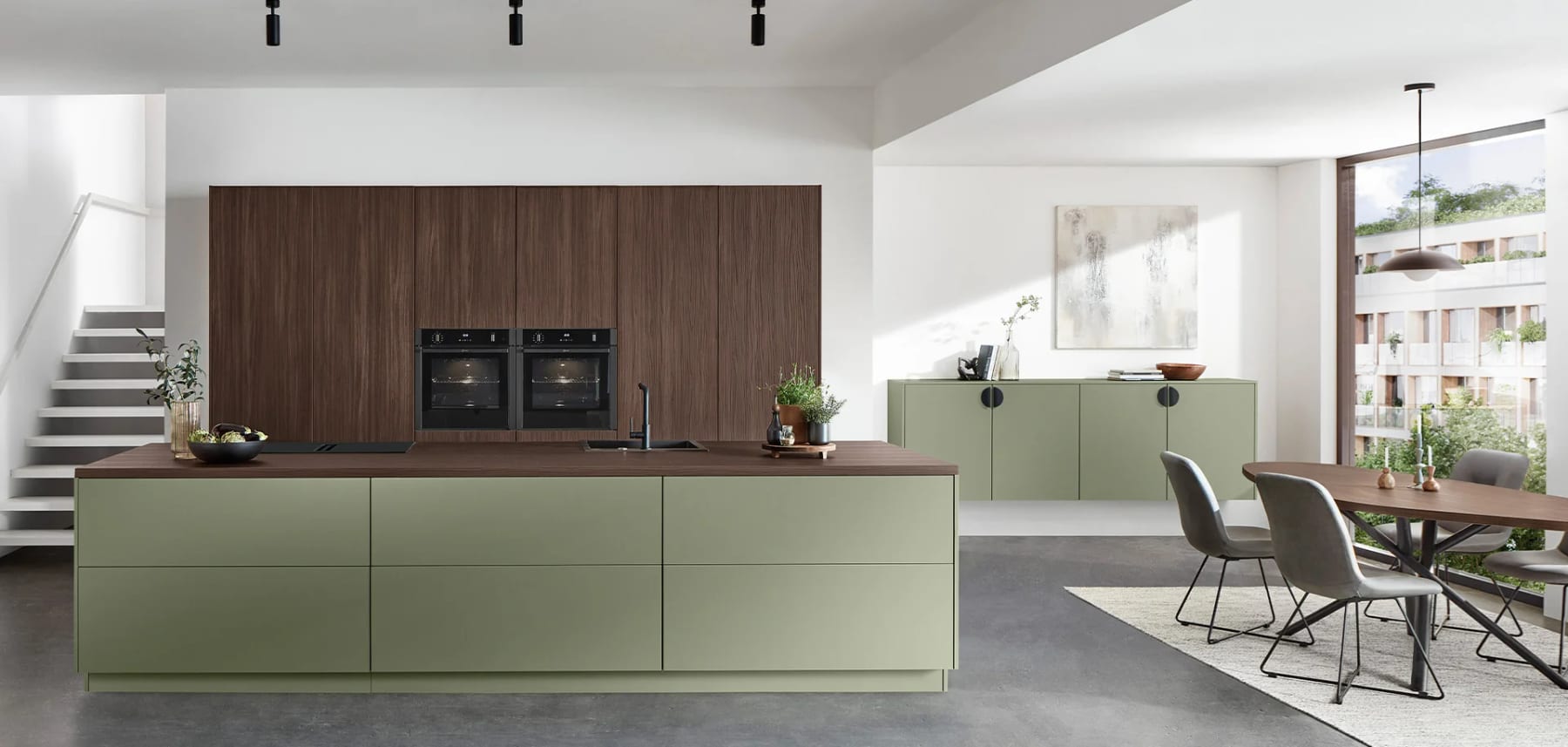 Îlot vert olive sans poignée devant une colonne en décor noyer, table de repas et escalier dans le prolongement de la pièce