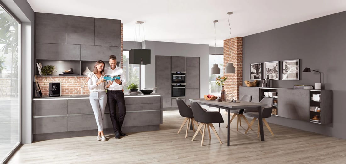 Cuisine linéaire en décor béton gris sans poignée le long d’un mur de brique, table de repas et meuble suspendu assorti dans la même pièce