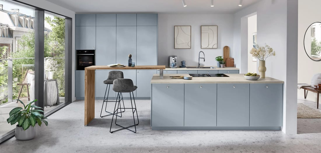 Cuisine bleu ciel mate à îlot dans un séjour clair, colonnes hautes et table haute en décor chêne