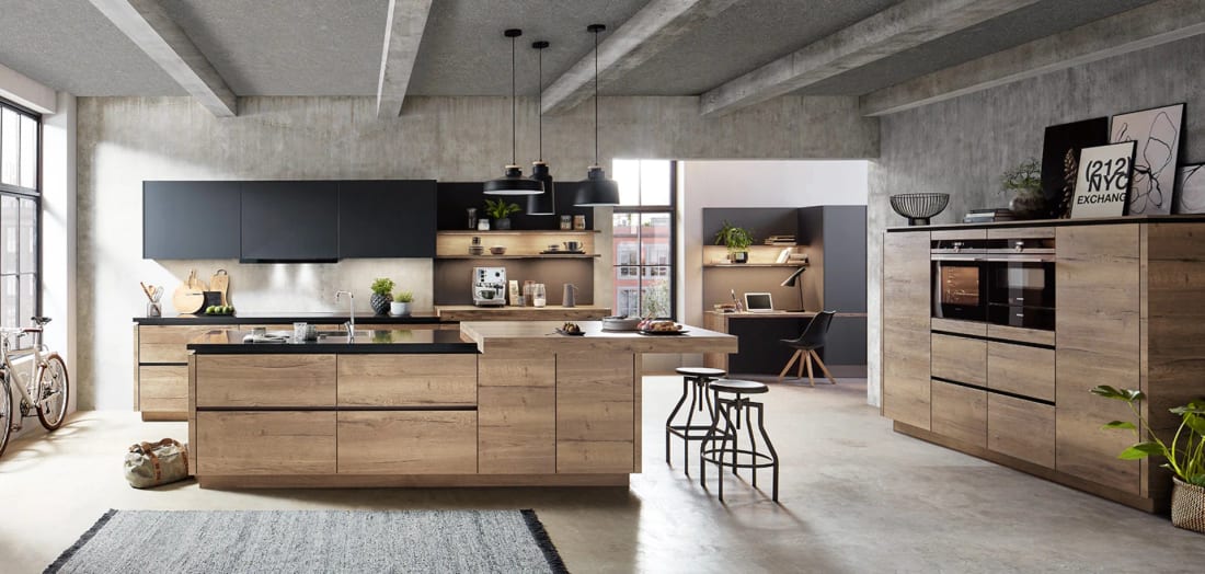 Cuisine à îlot en décor chêne Havane ouverte sur un coin bureau intégré aux mêmes meubles